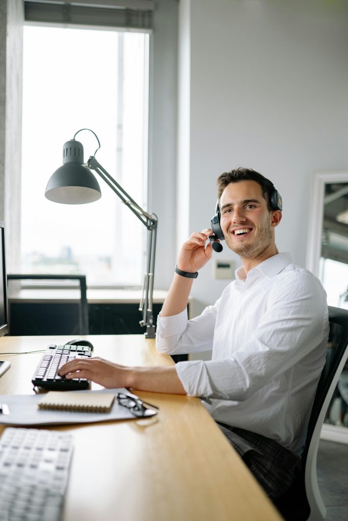 A cheerful call center agent wearing headphones works at a modern office desk.